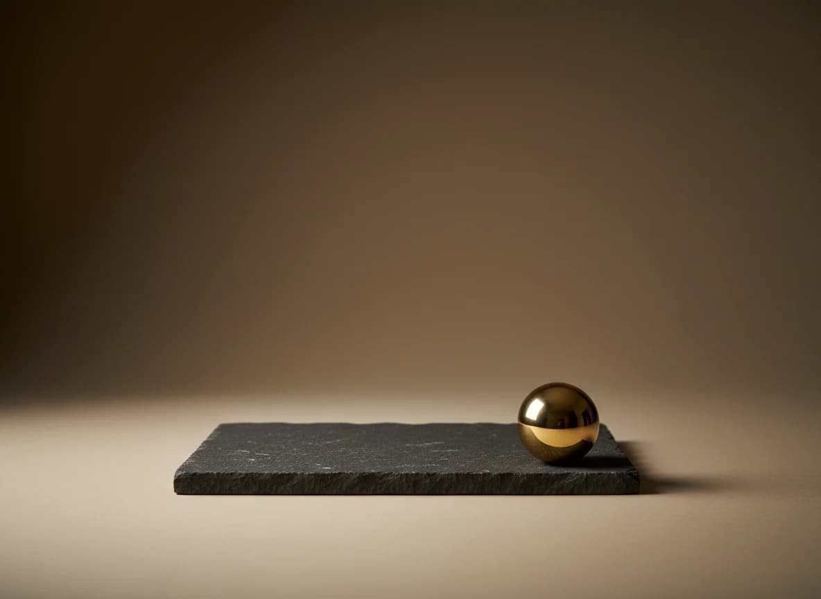 A polished brass sphere resting at one end of a flat charcoal stone slab