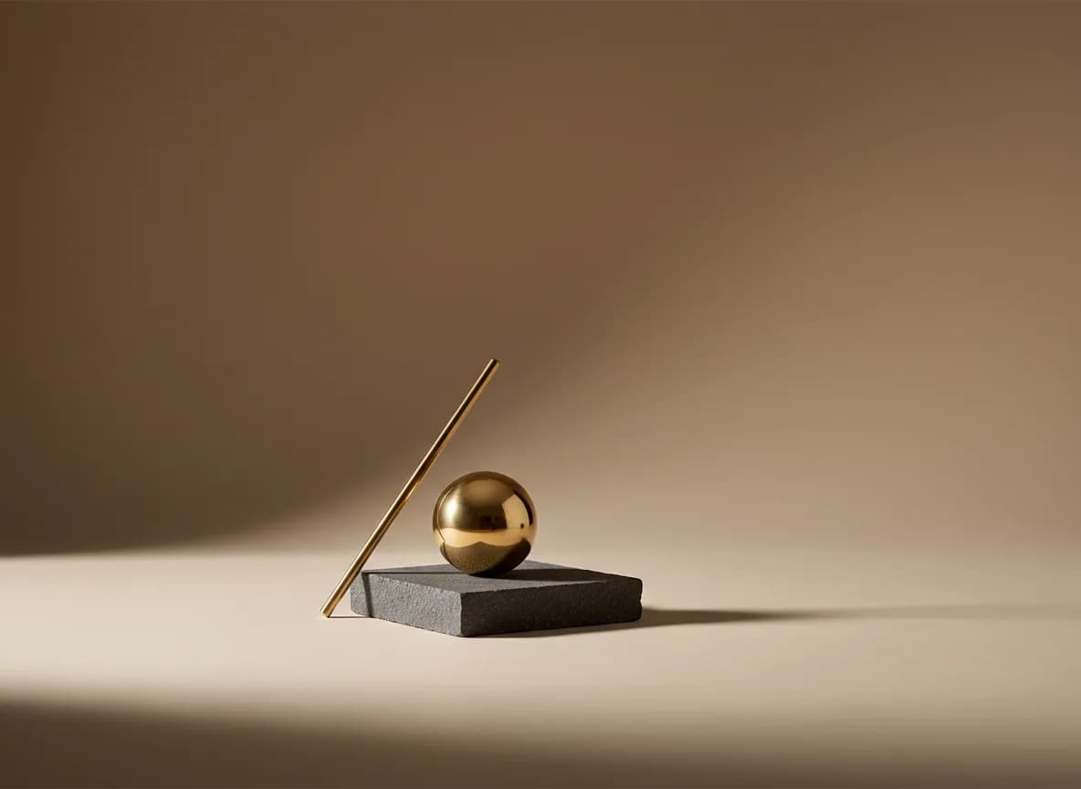 A single brass sphere resting on a low charcoal stone slab with a thin brass rod leaning against it