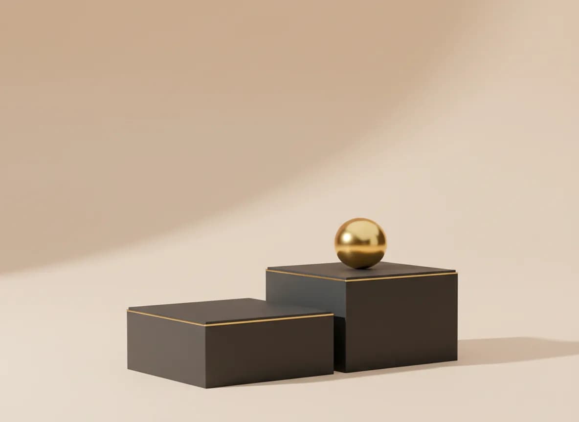 Two matte graphite plinths side by side, a polished gold sphere resting on the taller one
